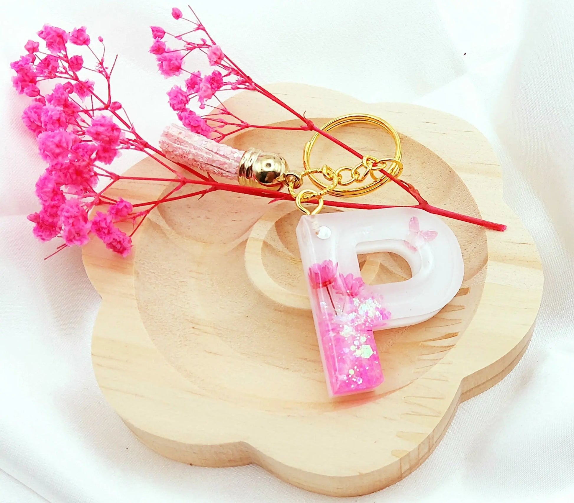 Porte-clés LETTRE P en résine époxy. Fond blanc. Paillettes, fleurs et papillon roses. Pompon gland pailleté rose.  PRETTY RESINE