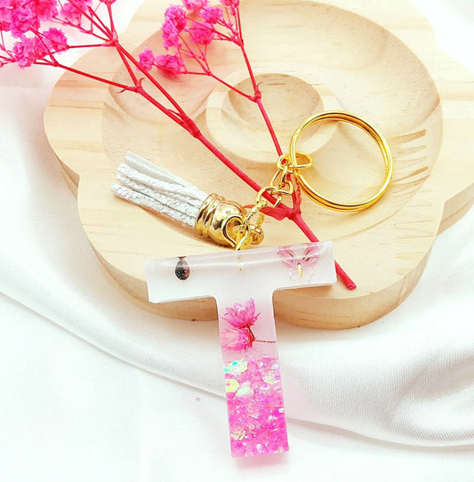 Porte-clés LETTRE T en résine époxy. Fond blanc, paillettes, fleurs et papillon roses. Pompon gland pailleté blanc. PRETTY RESINE