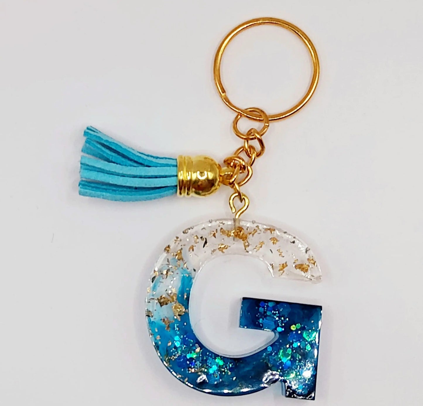 Porte-clés Lettre G en résine époxy, feuille d'or et paillettes bleues. Anneau doré. Pompon gland bleu ciel.