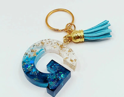 Porte-clés Lettre G en résine époxy, feuille d'or et paillettes bleues. Anneau doré. Pompon gland bleu ciel.