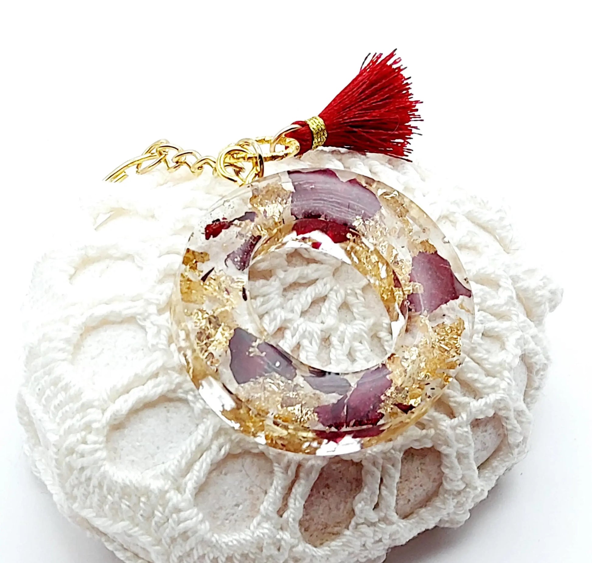 Porte-clés "Lettre O" en résine époxy, pétales de roses et feuille d'or. Pompon gland rouge, anneau doré. Posé sur un galet