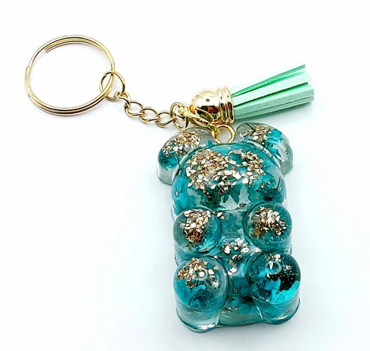 Porte-clés "Ourson debout" en résine époxy. Fleurs turquoises et verre pilé doré. Anneau doré et pompon gland vert pastel.