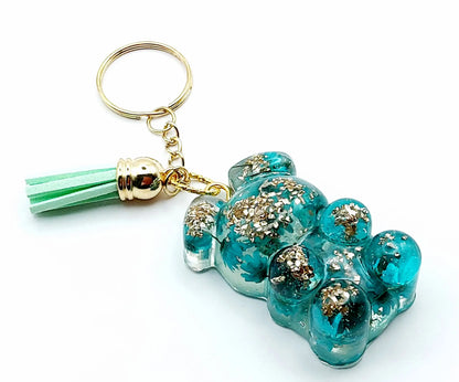 Porte-clés "Ourson debout" en résine époxy. Fleurs turquoises et verre pilé doré. Anneau doré et pompon gland vert pastel.