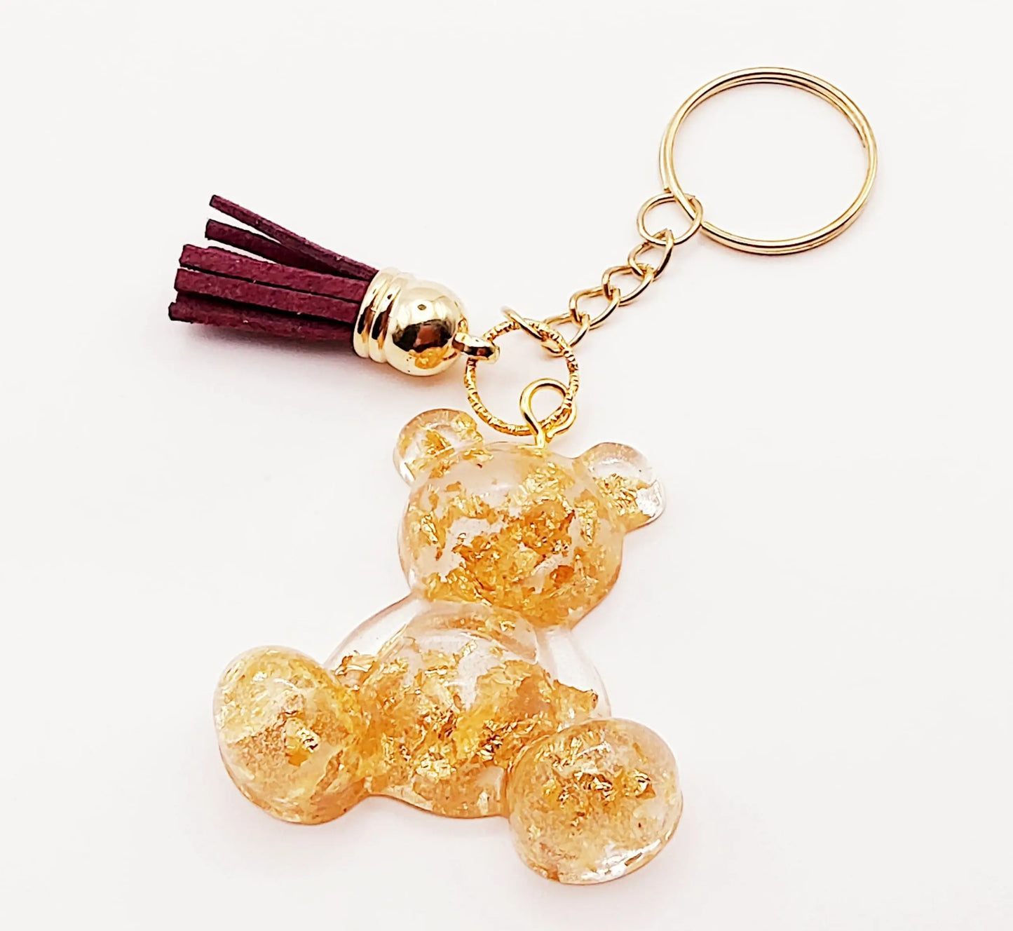 Porte-clés "Ourson assis" en résine époxy. Transparent avec feuille d'or. Anneau doré. Pompon gland prune.