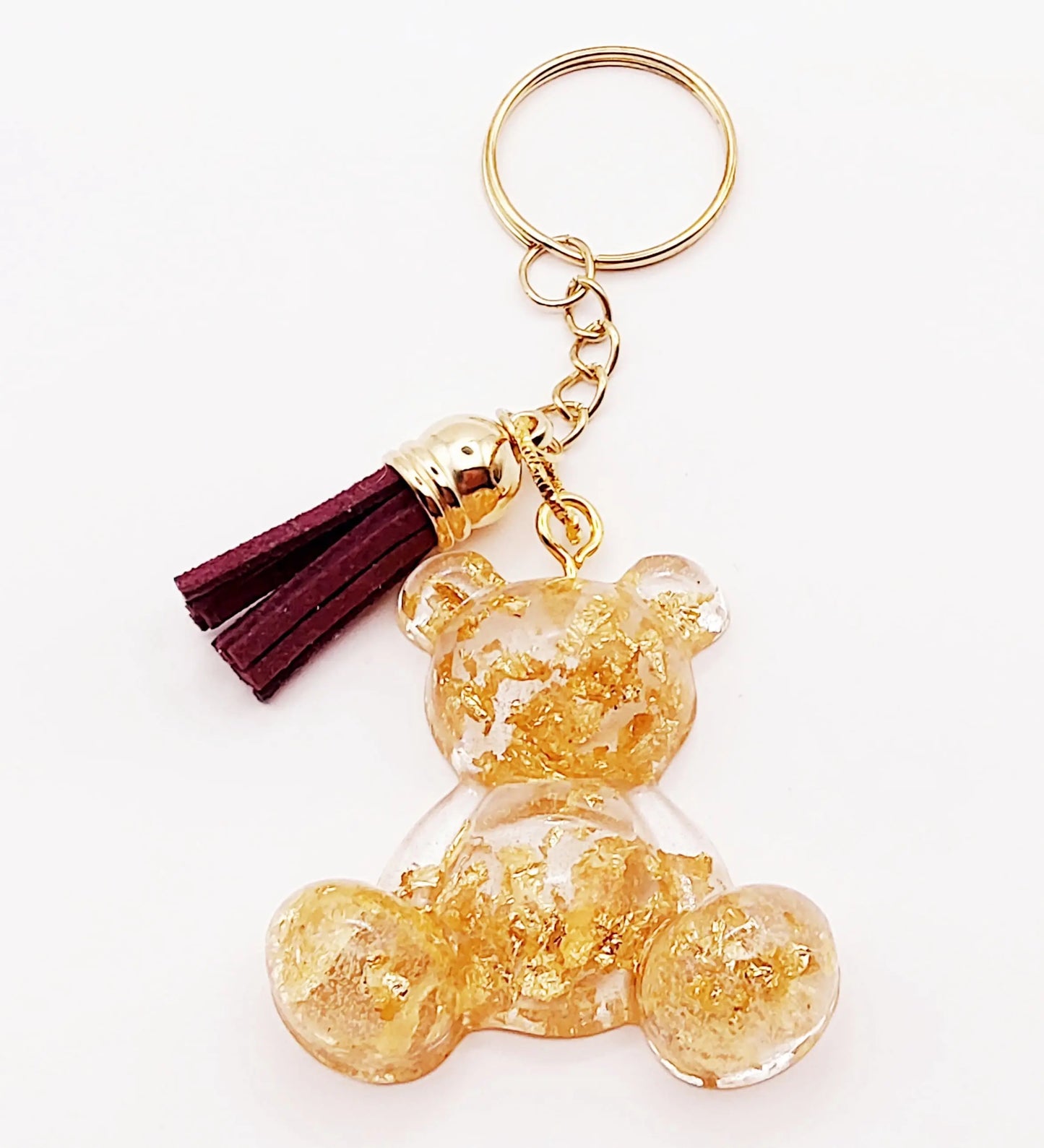 Porte-clés "Ourson assis" en résine époxy. Transparent avec feuille d'or. Anneau doré. Pompon gland prune.