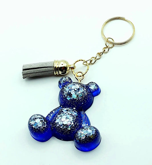 Porte-clés "Ourson assis" en résine époxy, bleu marine et paillettes argentées. Anneau doré. Pompon gland gris clair.