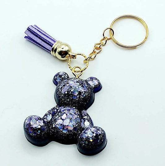 Porte-clés "Ourson assis" en résine époxy, violet et paillettes mauves. Anneau doré, pompon gland mauve.