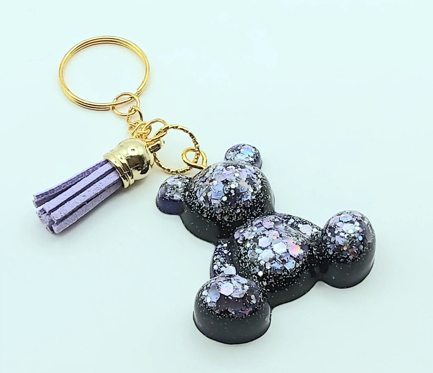 Porte-clés "Ourson assis" en résine époxy, violet et paillettes mauves. Anneau doré, pompon gland mauve.