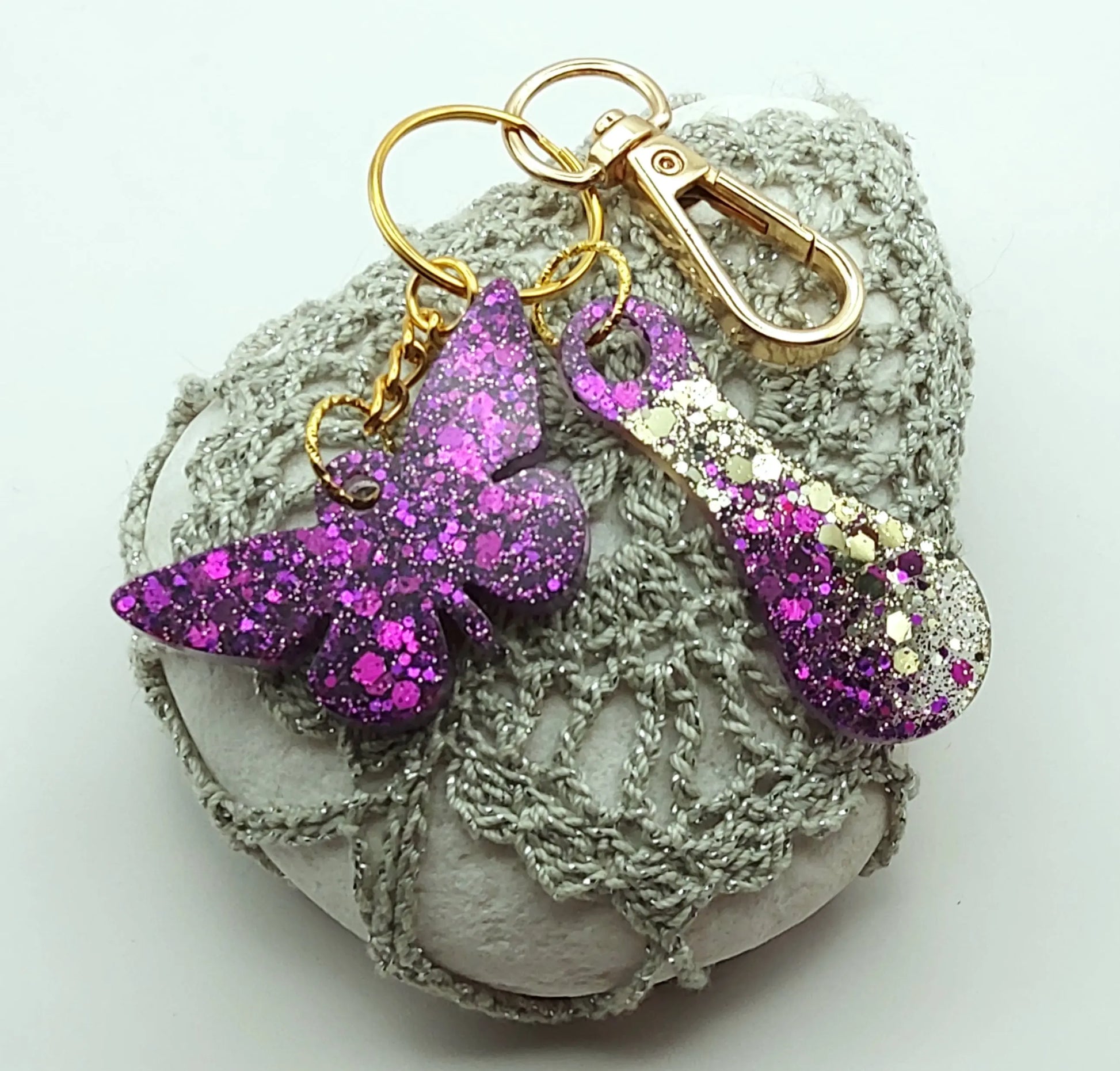 Porte-clés "Papillon et jeton de caddie" en résine époxy, paillettes violettes, anneau et mousqueton dorés, posé sur un galet