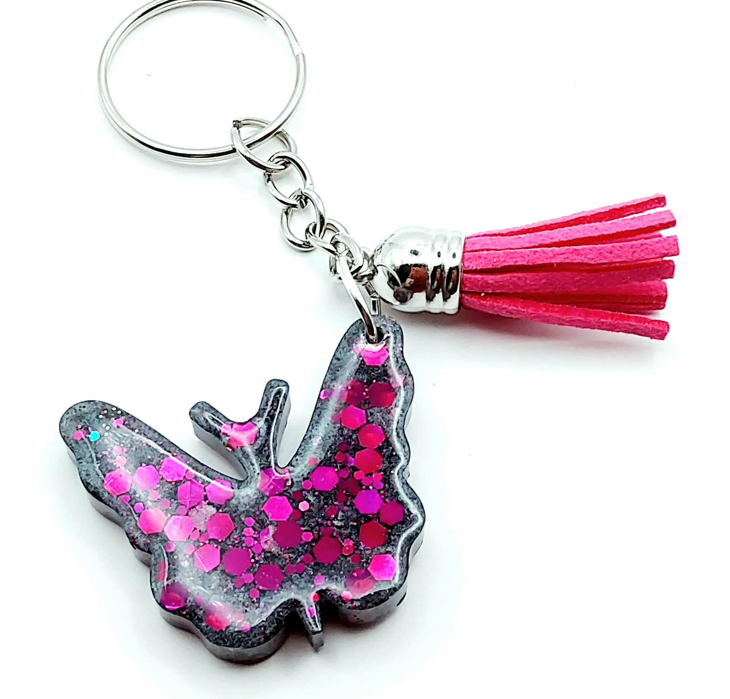 Porte-clés "Papillon" en résine époxy, gris et paillettes fuchsia. Anneau argenté. Pompon gland fuchsia.