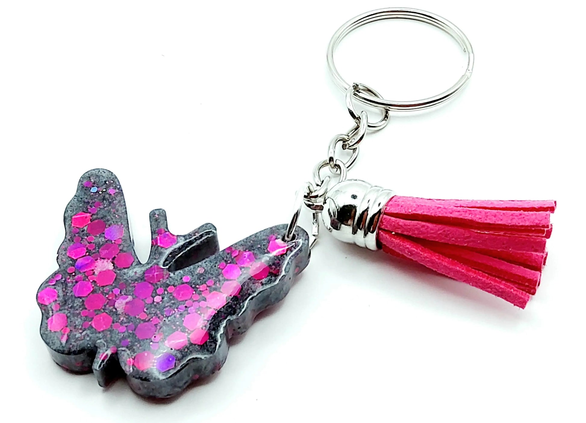 Porte-clés "Papillon" en résine époxy, gris et paillettes fuchsia. Anneau argenté. Pompon gland fuchsia.