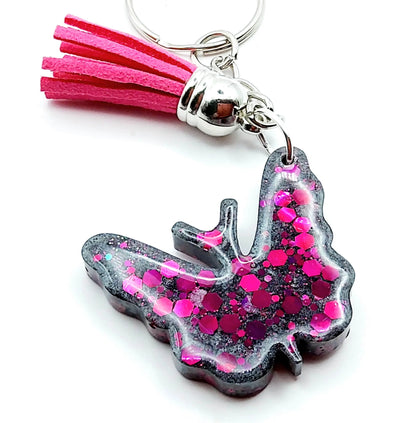 Porte-clés "Papillon" en résine époxy, gris et paillettes fuchsia. Anneau argenté. Pompon gland fuchsia.