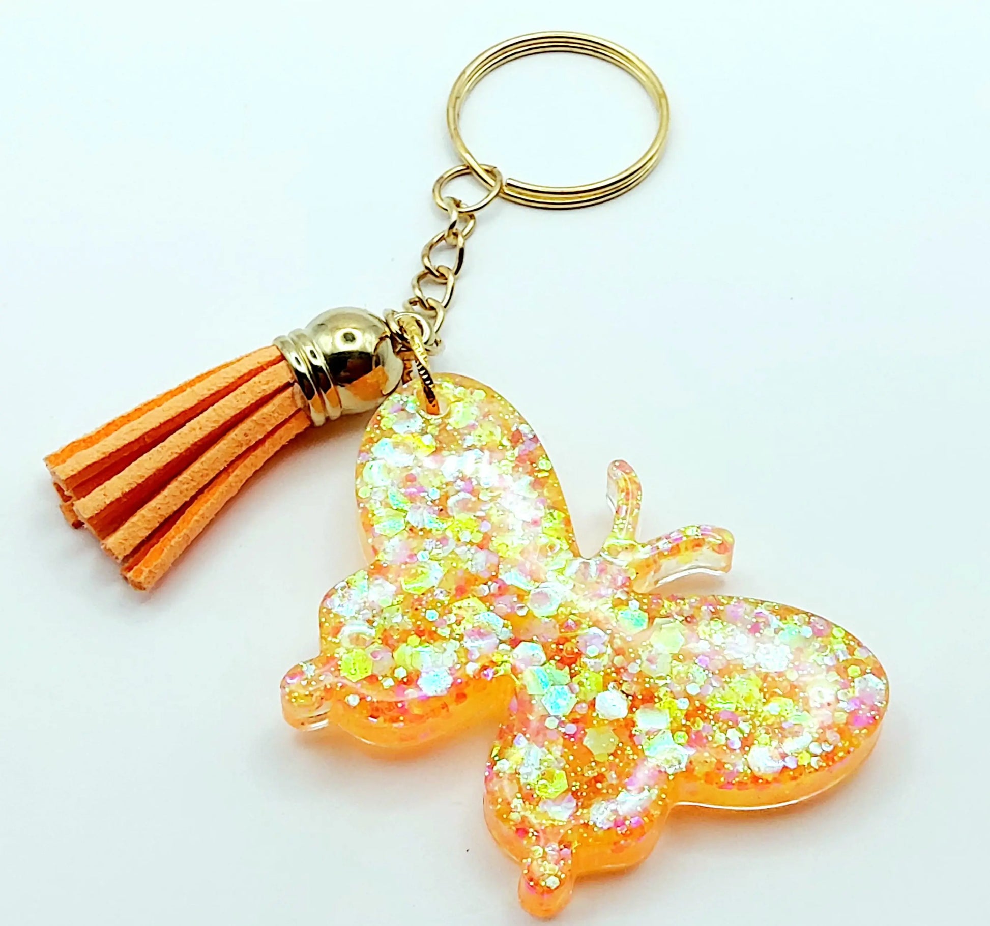 Porte-clés "Papillon" en résine époxy. Paillettes oranges et jaunes. Anneau doré. Pompon gland orange.