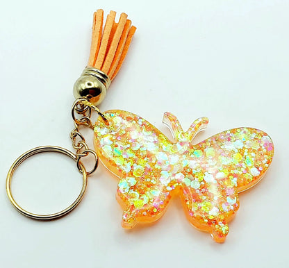 Porte-clés "Papillon" en résine époxy. Paillettes oranges et jaunes. Anneau doré. Pompon gland orange.