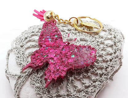 Porte-clés "Papillon" en résine époxy, paillettes et pompon roses fuchsia, posé sur un galet