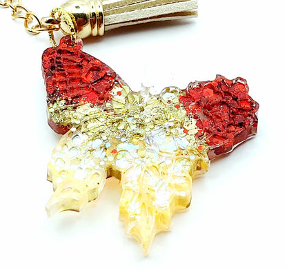 Porte-clés "Papillon" en résine époxy, paillettes rouges et or. Anneau doré, pompon gland beige. Gros plan.