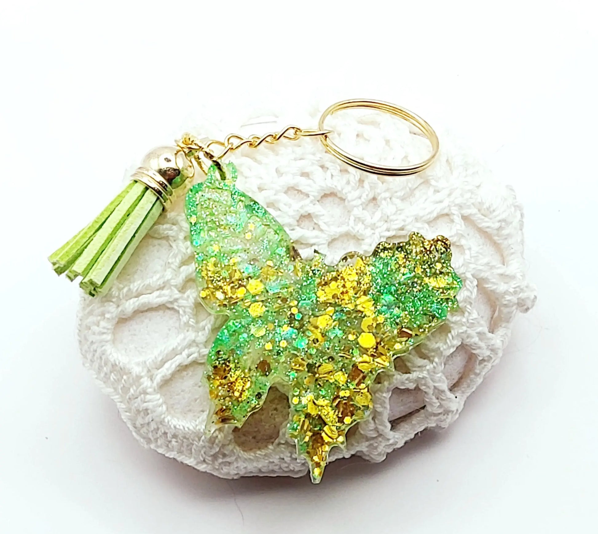 Porte-clés "Papillon" en résine époxy. Paillettes vertes et dorées, pompon gland vert, anneau doré. Posé sur un galet.