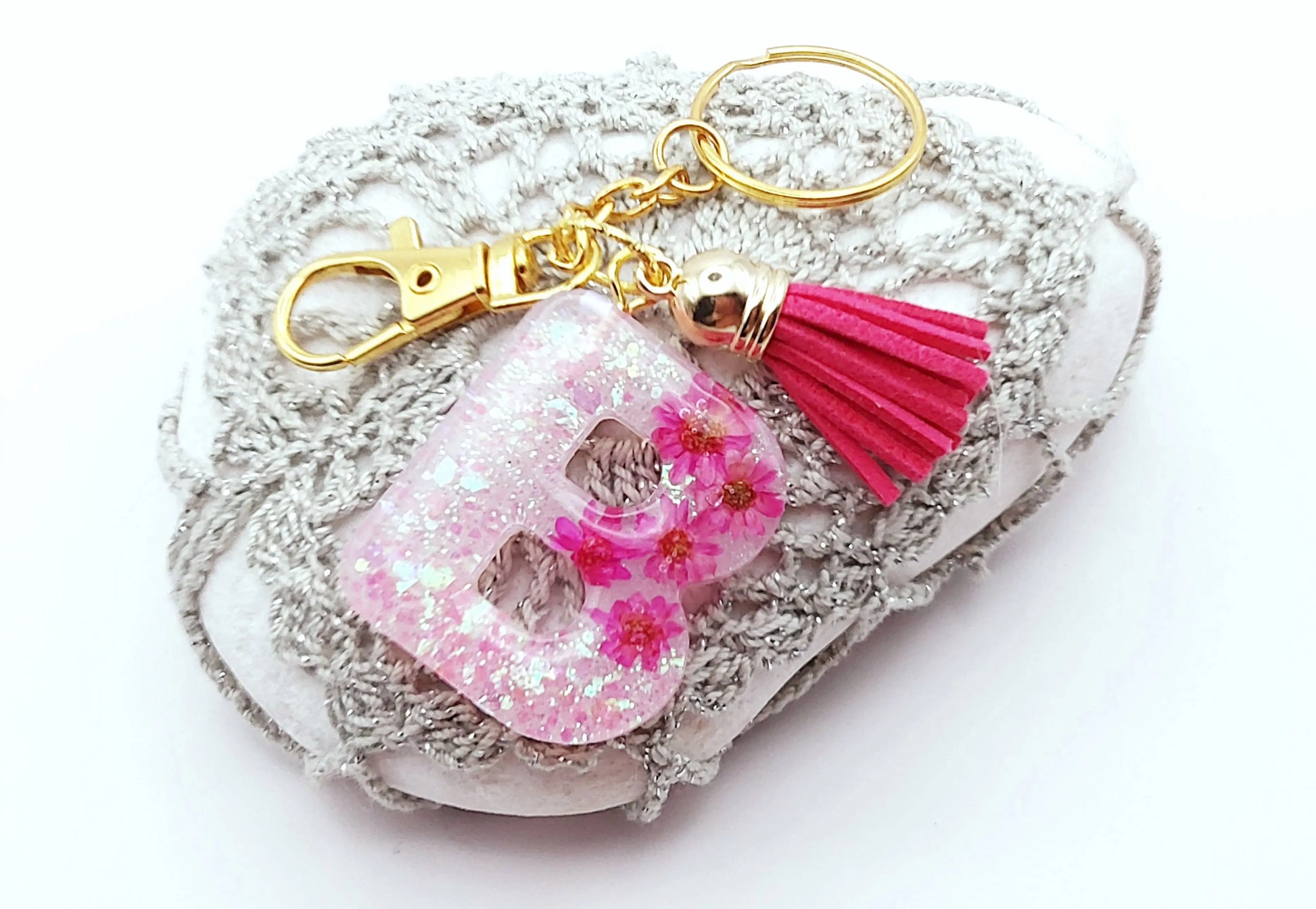 Porte-clés "Petite Lettre B" en résine époxy, Fleurs roses fuchsia et paillettes holographiques blanches, posé sur un galet