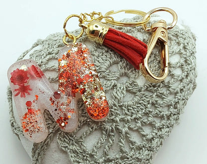 Porte-clés "Petite Lettre M" en résine époxy, fleurs rouges, paillettes rouges et or, posé sur un galet