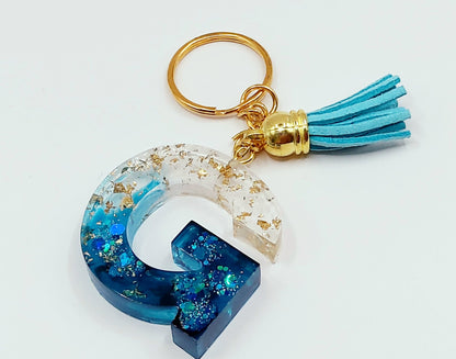 Porte-clés Lettre G en résine époxy, feuille d'or et paillettes bleues. Anneau doré. Pompon gland bleu ciel.