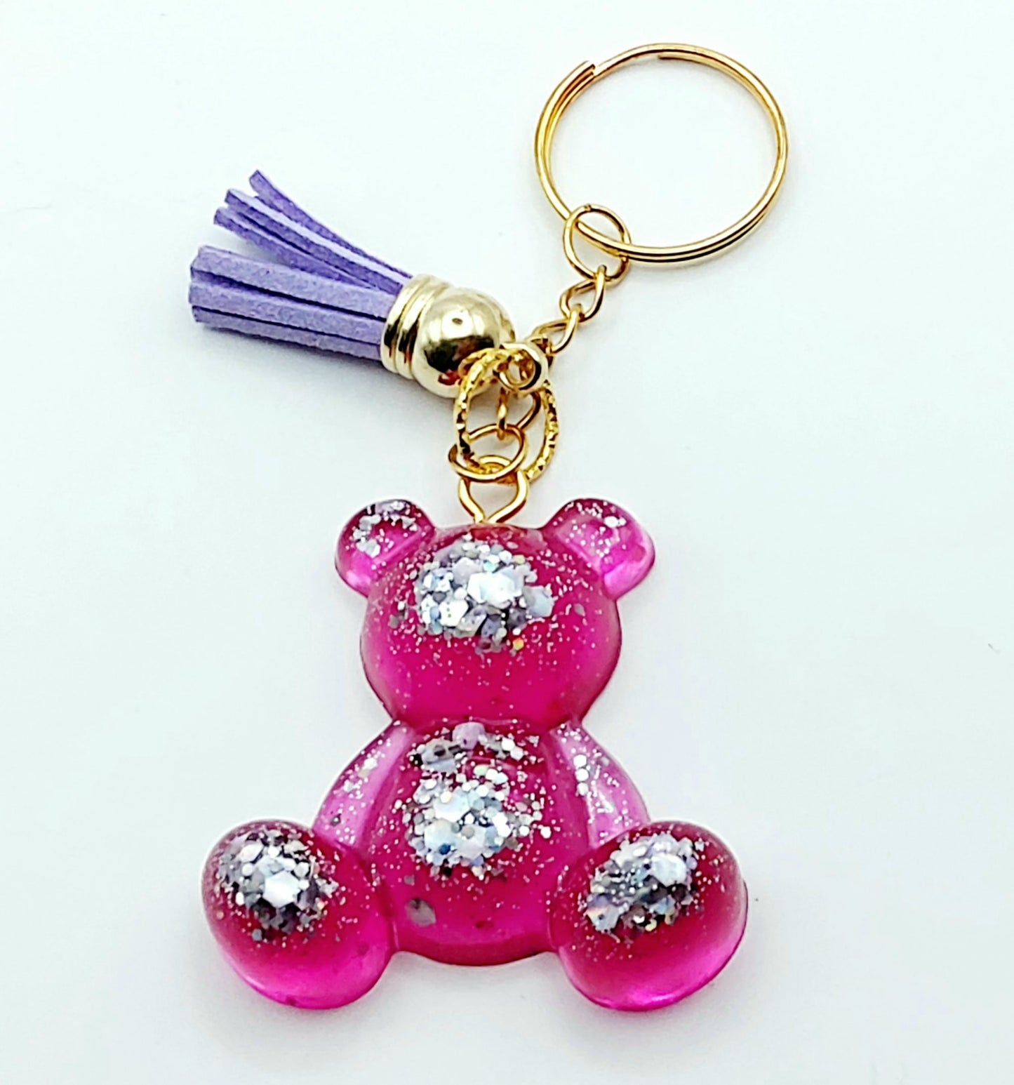 Porte-clés "Ourson assis" en résine époxy, rose et paillettes argentées. Anneau doré, pompon gland mauve.