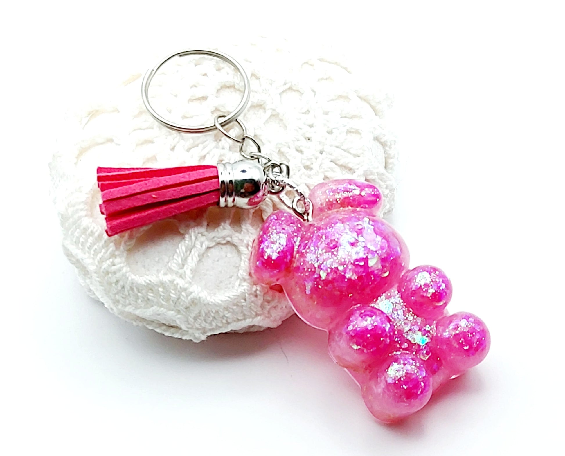 Porte-clés "Ourson debout" en résine époxy, paillettes holographiques roses, pompon gland fuchsia, anneau argenté. Posé sur un galet.