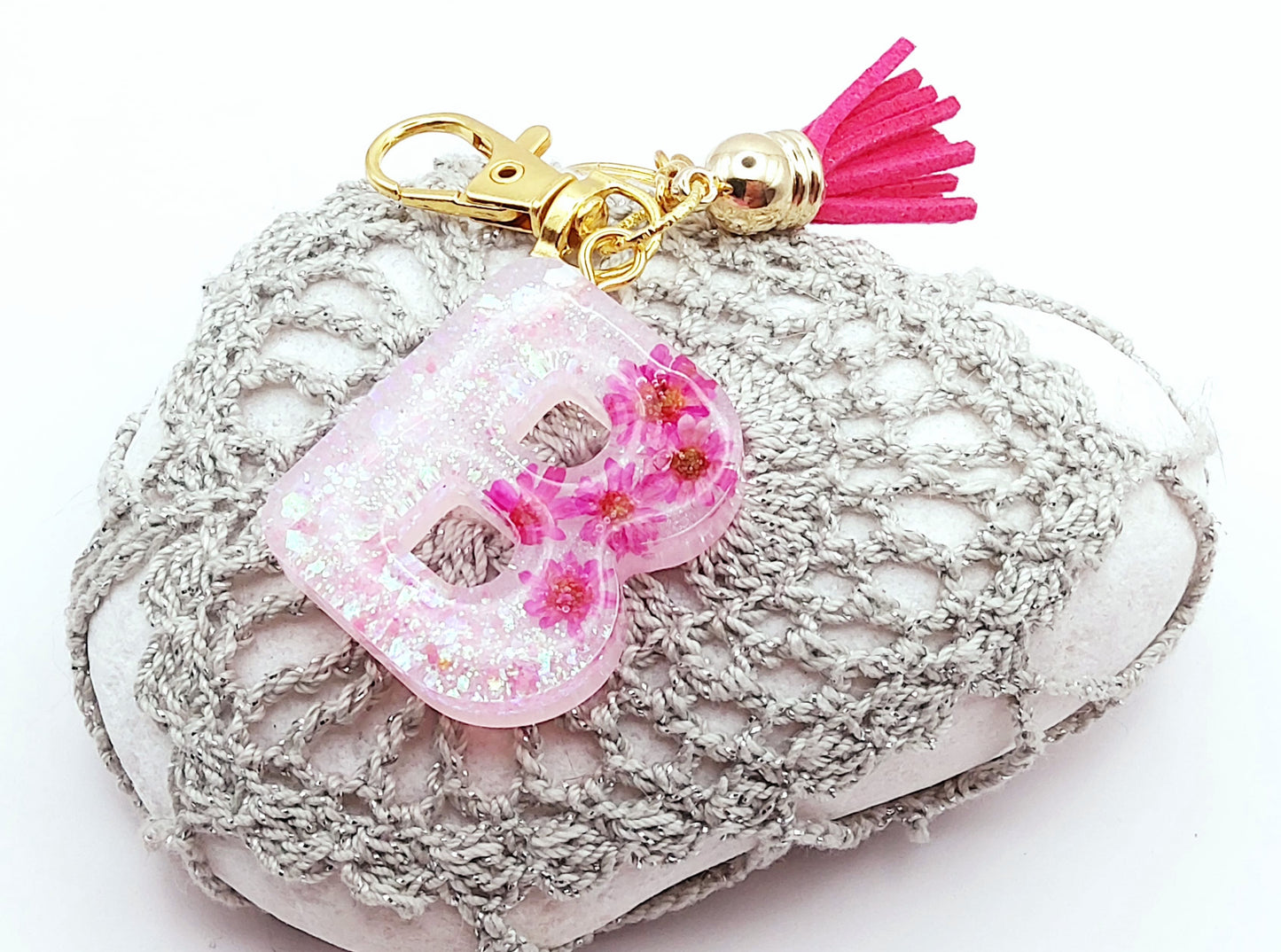 Porte-clés "Petite Lettre B" en résine époxy, Fleurs roses fuchsia et paillettes holographiques blanches, posé sur un galet