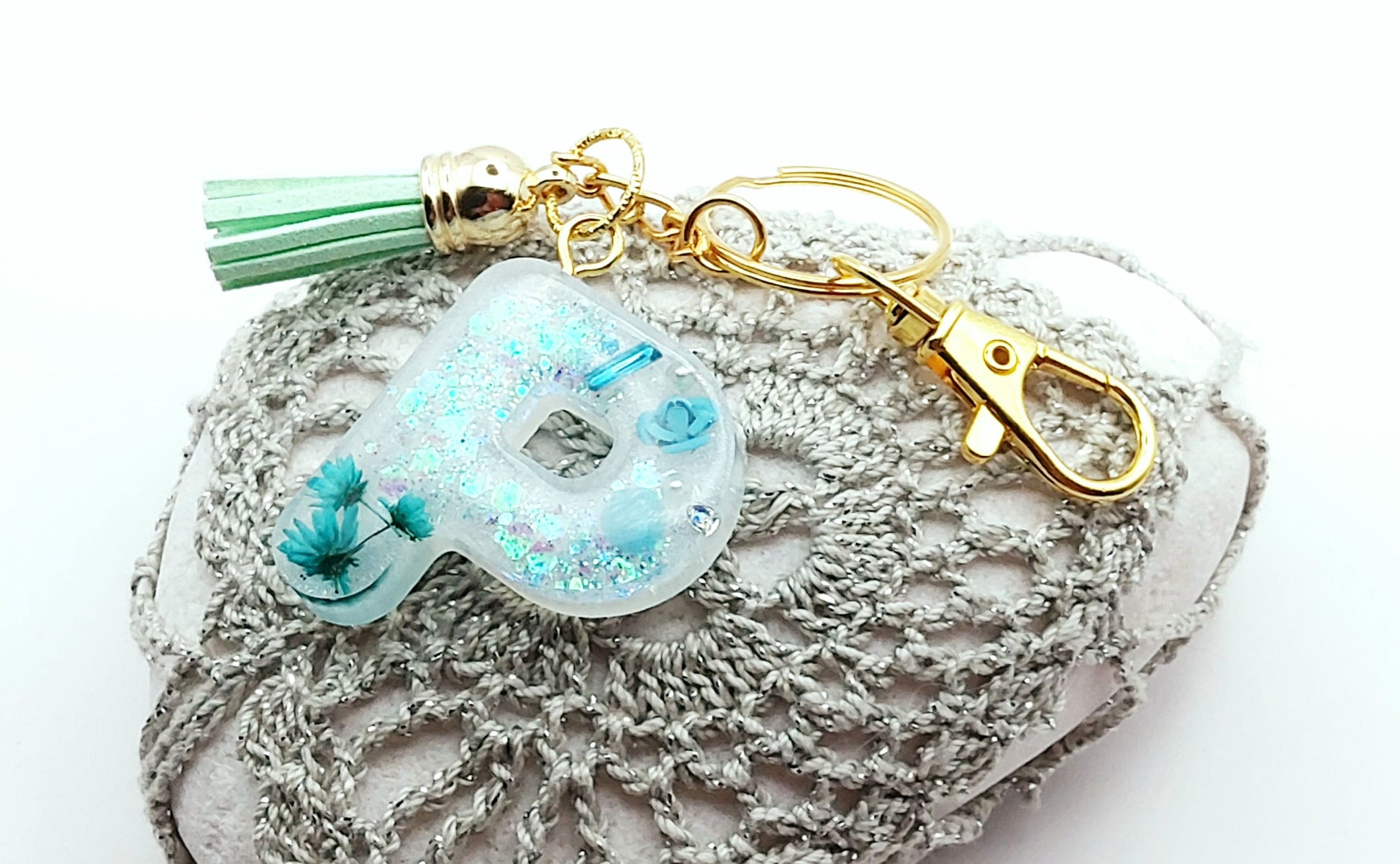 Porte-clés "Petite Lettre P" en résine époxy, fleurs turquoise, pompon gland vert pastel, posé sur un galet