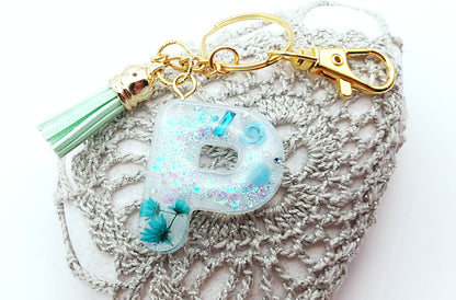 Porte-clés "Petite Lettre P" en résine, fleurs turquoise, pompon gland vert pastel, posé sur un galet